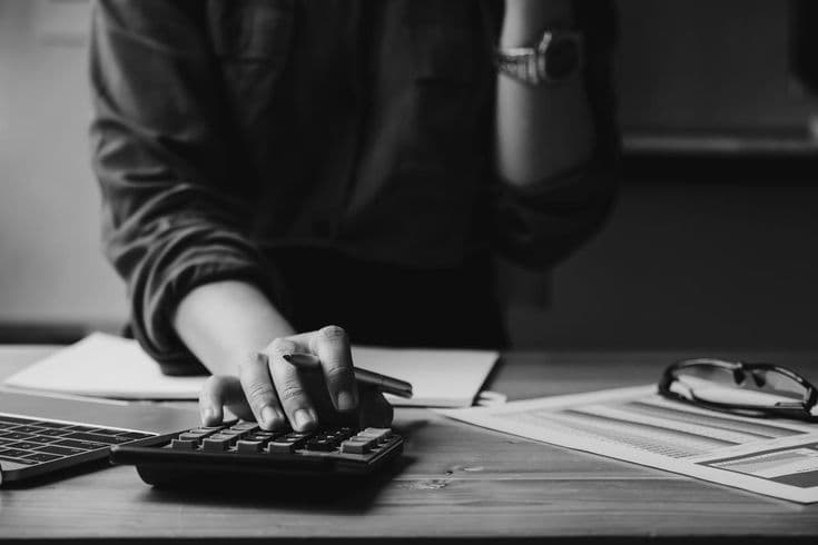 Black and white close-up of hands using a calculator and pen with financial documents.