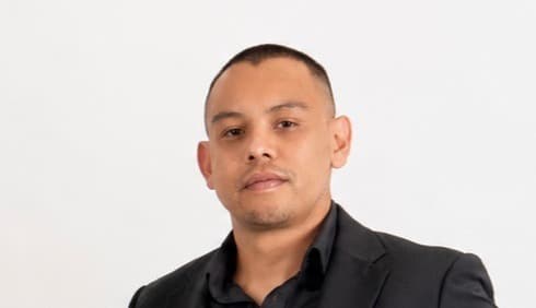Man with short hair wearing a black blazer and shirt against a white background.
